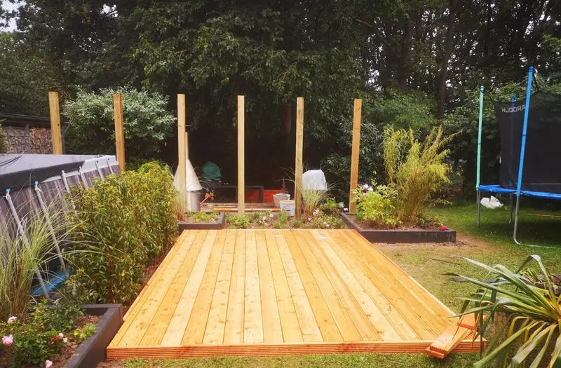 Dasselbe Terrassenprojekt fertiggestellt: Holzterrasse mit eingewachsenen Hochbeeten und Pergola