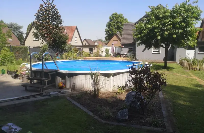 Rund angelegter Gartenpool mit Holz-Einstieg und neu bepflanztem Beet mit Findling