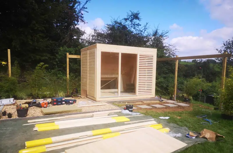 Aufbau eines Sauna-Gartenhauses aus hellem Holz mit Glasfront im Garten